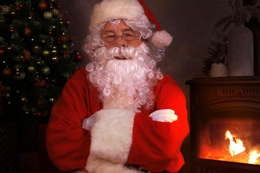 Traditional Santa Claus standing by the fireplace and Christmas tree in a room