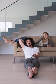 Young couple relaxes on the sofa in the luxury living room, using a tablet and remote control