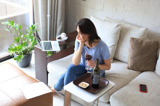 Successful young beautiful woman sitting on a sofa in the living room, drinking red wine