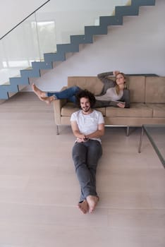 Young couple relaxes on the sofa in the luxury living room, using a tablet and remote control