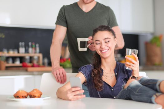 Happy couple using smartphone sitting in kitchen.