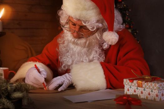 Portrait of happy Santa Claus sitting at his room at home near Christmas tree and answering Christmas letters