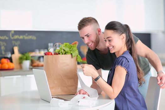 Couple paying their bills with laptop in kitchen at home.