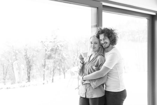 romantic happy young couple enjoying morning coffee by the window on cold winter day at home