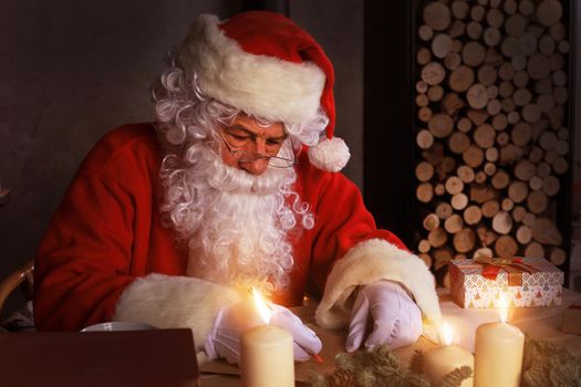 Portrait of happy Santa Claus sitting at his room at home near Christmas tree and answering Christmas letters