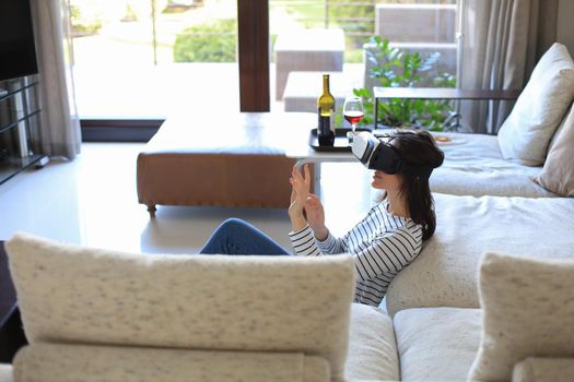 Young casual girl wearing VR headset while lounging on the floor near couch at home and looking around