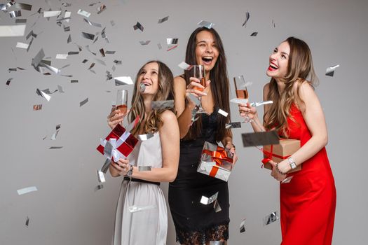 beautiful female friends in dresses with champagne and a lot of confetti around them, isolated on white background