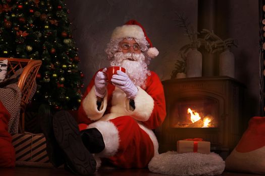Santa Claus having a rest in a comfortable chair near the fireplace at home
