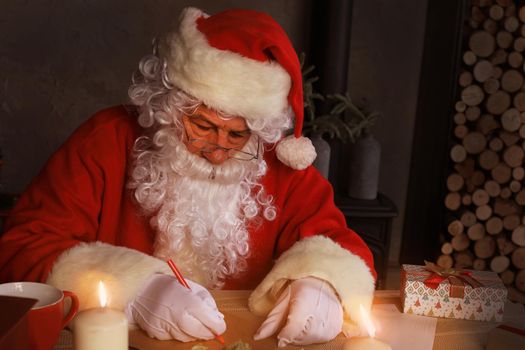 Portrait of happy Santa Claus sitting at his room at home near Christmas tree and answering Christmas letters