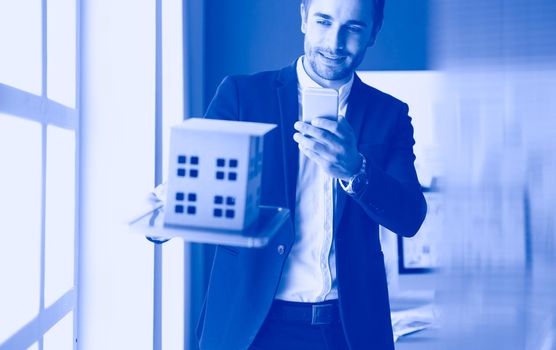 Businessman holding house miniature on hand standing in office