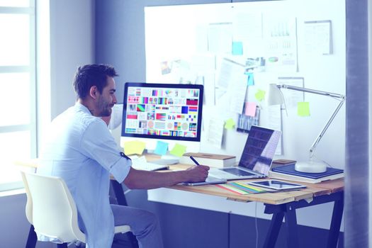 Portrait of young designer sitting at graphic studio in front of laptop and computer while working online