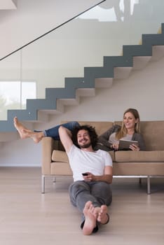 Young couple relaxes on the sofa in the luxury living room, using a tablet and remote control