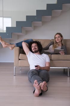 Young couple relaxes on the sofa in the luxury living room, using a tablet and remote control