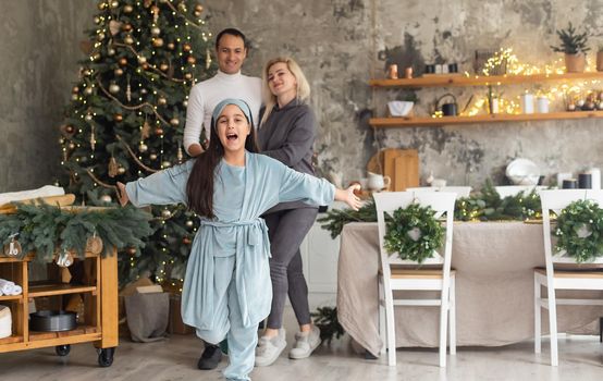 Christmas Family. Happiness. Portrait of dad, mom and daughter at home near the Christmas tree, all are smiling.