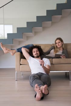 Young couple relaxes on the sofa in the luxury living room, using a tablet and remote control