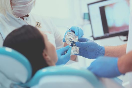 Senior male dentist in dental office talking with female patient and preparing for treatment.