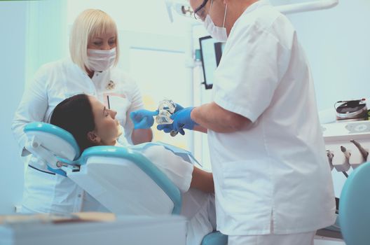 Senior male dentist in dental office talking with female patient and preparing for treatment.