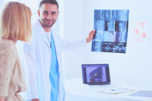 Handsome doctor is talking with young female patient and making notes while sitting in his office