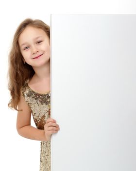 A nice little girl is looking because of an empty banner in which you can insert any text. The concept of a happy childhood, advertising, selling goods. Isolated on white background.