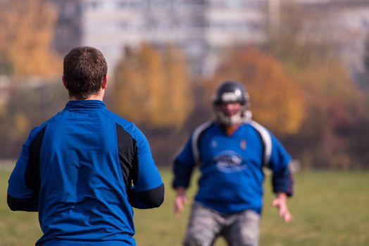 Team coach throwing the ball into the group of young american football players in action during the training at the field