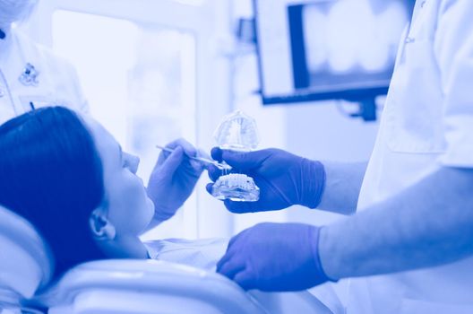 Senior male dentist in dental office talking with female patient and preparing for treatment.