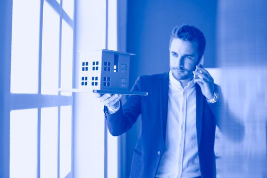 Businessman holding house miniature on hand standing in office