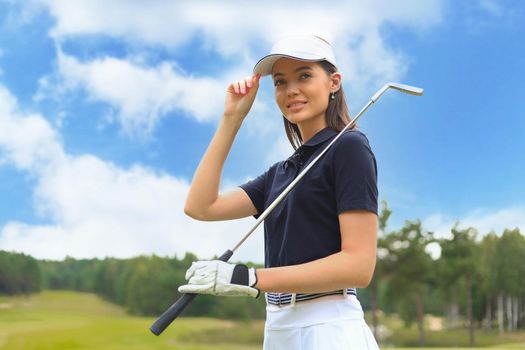 Professional female golfer holding golf club on field and looking away. Young woman standing on golf course on a sunny day.