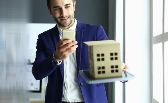 Businessman holding house miniature on hand standing in office