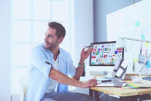 Portrait of young designer sitting at graphic studio in front of laptop and computer while working online