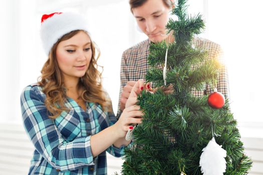 family, x-mas, winter holidays and people concept - happy young couple decorating christmas tree at home.