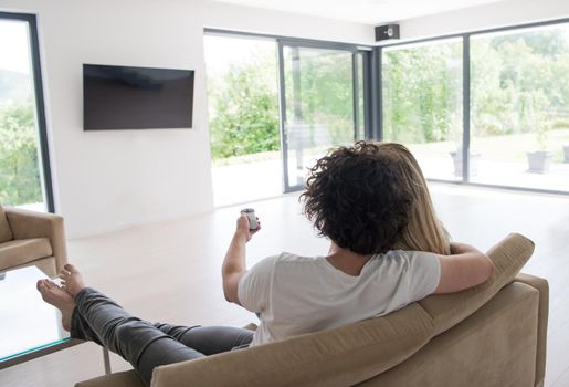 Rear view of couple watching television in living room their luxury home