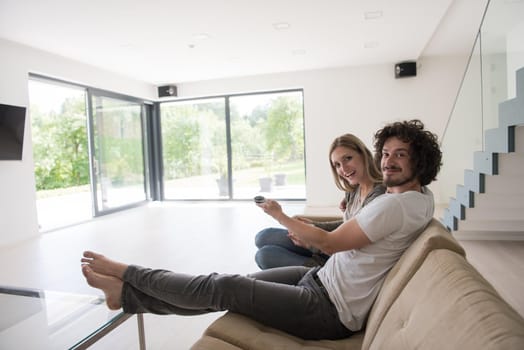 Young couple relaxes on the sofa in the luxury living room, using a tablet and remote control