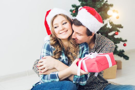 Family, x-mas, winter holidays and people concept - happy couple hugging near christmas tree at home.