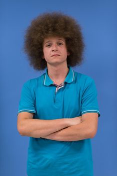 portrait of a young man with a funky hairstyle with arms crossed on blue background