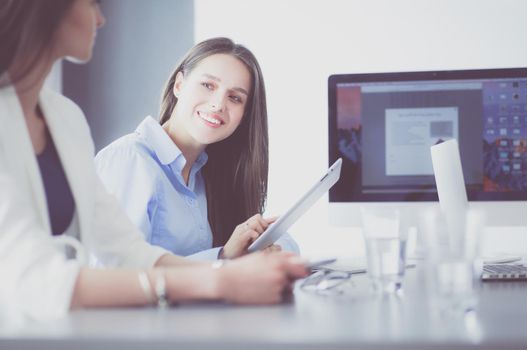 Two female colleagues in office sitting on the desk.