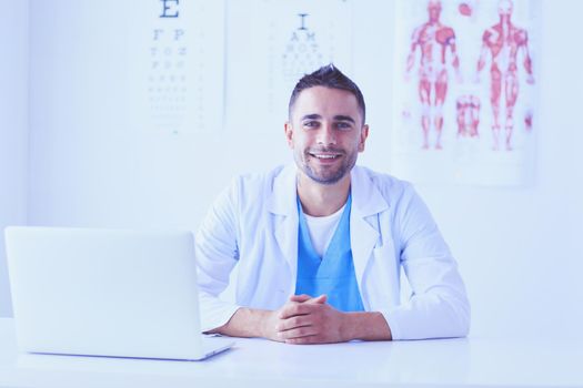 Portrait of a male doctor with laptop sitting at desk in medical office