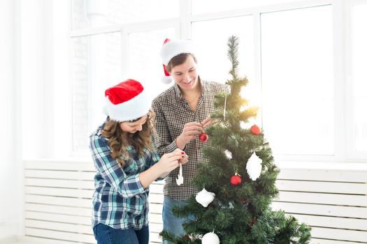 family, x-mas, winter holidays and people concept - happy young couple decorating christmas tree at home.