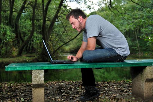 one young businessman working on laptop outdoor with green nature in background