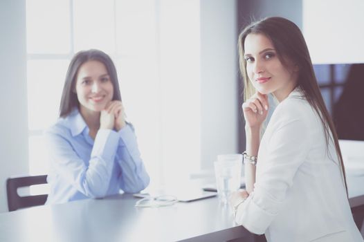 Two female colleagues in office sitting on the desk.