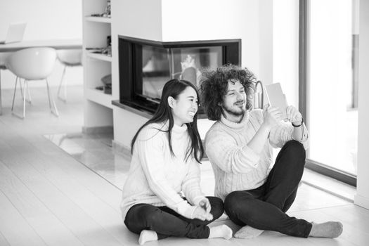 beautiful young multiethnic couple using tablet computer in front of fireplace on cold winter day at home