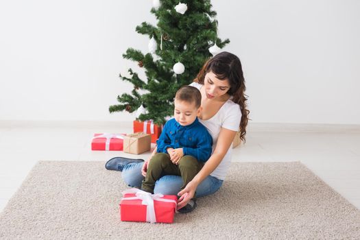 Christmas, single parent and holidays concept - Cute little boy holding christmas present for his mother at the home