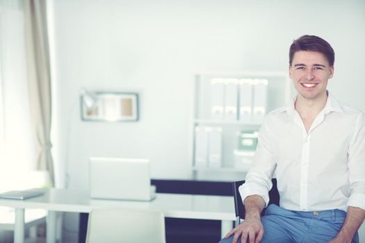 Happy young business man sitting at desk in office.