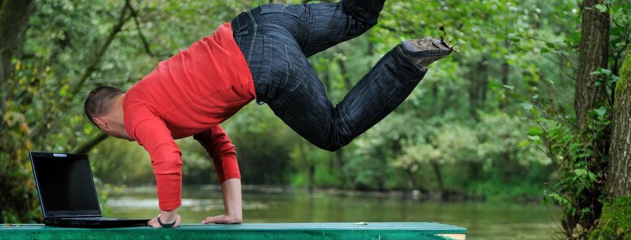 young businessman jump over edge with laptop and green nature in background