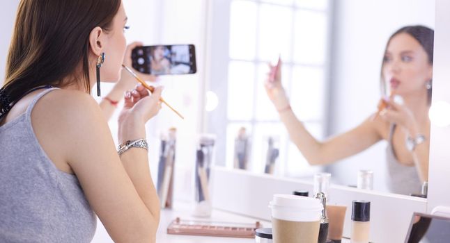 Beauty blogger filming makeup tutorial with smartphone in front of mirror .