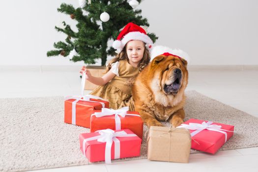 Children and pet concept - Cute girl with dog sitting near the Christmas tree. Merry Christmas and Happy Holidays