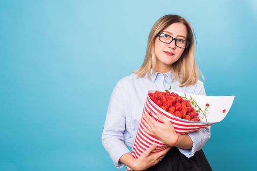 Young woman holding bouquet of strawberries on blue background.