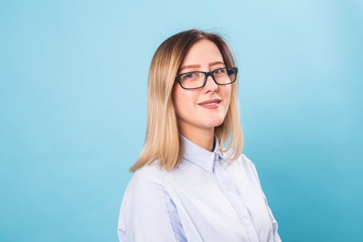 Cheerful beautiful young student woman with glasses over blue background.