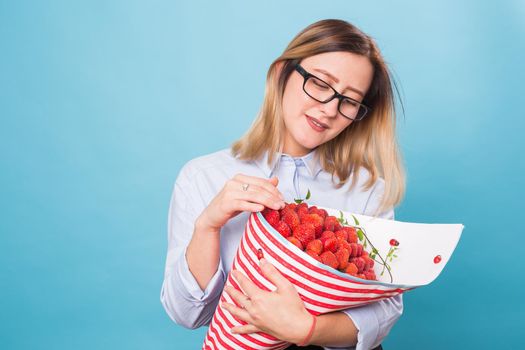 Young woman holding bouquet of strawberries on blue background.