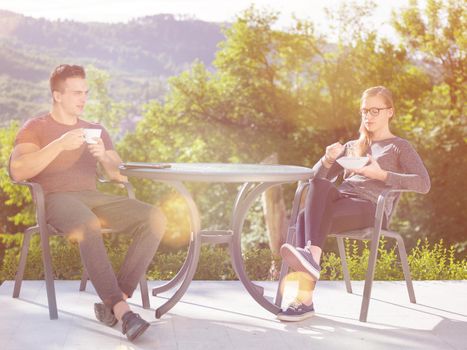 young beautiful handsome couple enjoying morning coffee and breakfast in front of their luxury home villa