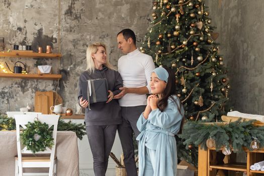 Christmas Family. Happiness. Portrait of dad, mom and daughter at home near the Christmas tree, all are smiling.